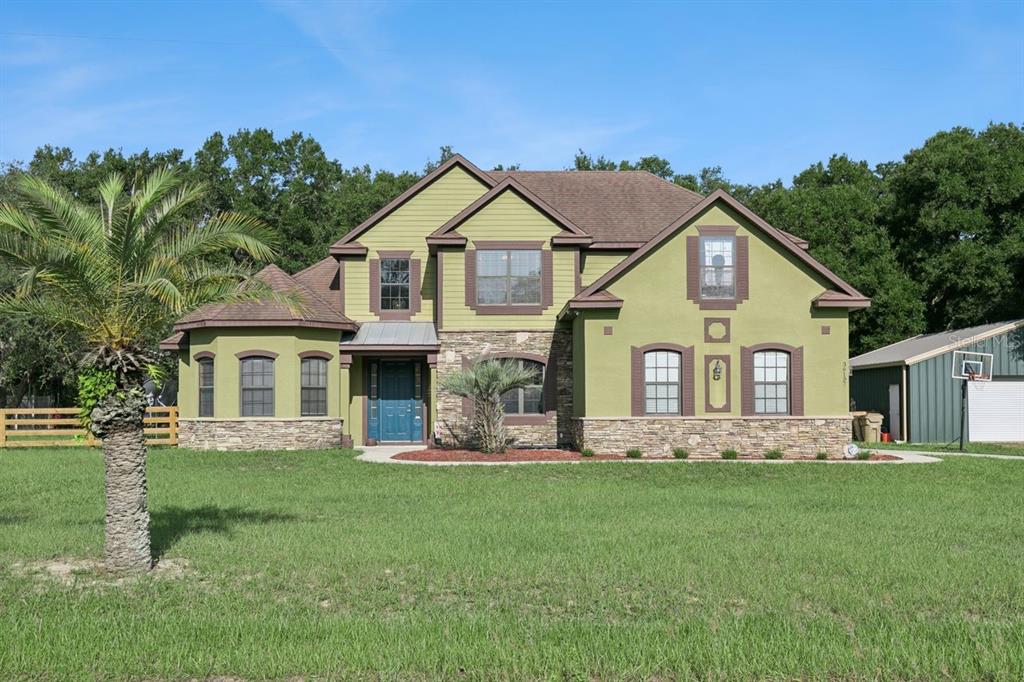 A two-story house with green siding, stone accents, and a front yard with a palm tree — 36137 MATTAWAN DRIVE, EUSTIS, FL