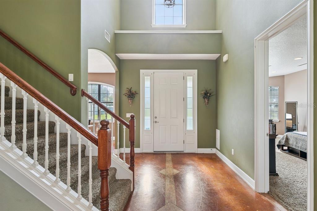 An entryway features a staircase with carpeted steps, a white front door, and stained concrete floors — 36137 MATTAWAN DRIVE, EUSTIS, FL