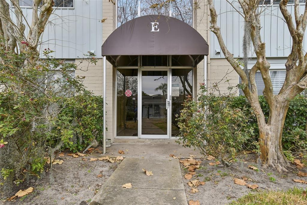 The exterior entrance of a building marked with the letter E features a brown awning — 1695 LEE ROAD UNIT E215, WINTER PARK, FL