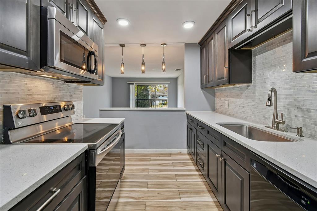 A galley kitchen features dark wood cabinets, stainless steel appliances, white countertops, and tile flooring — 1695 LEE ROAD UNIT E215, WINTER PARK, FL