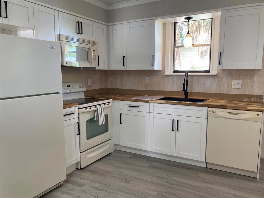 A kitchen features white cabinets, wood countertops, a glass dining table, and light wood flooring — 31 W OAKWOOD STREET UNIT 2, TARPON SPRINGS, FL