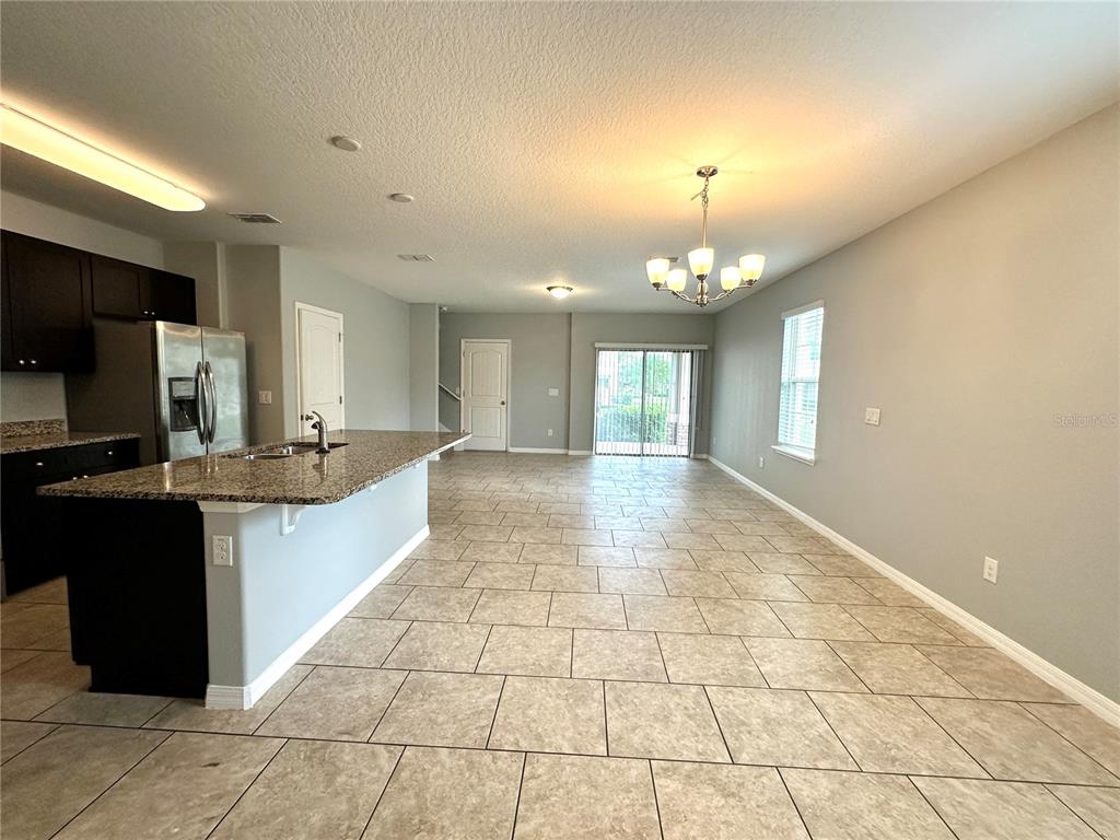 A kitchen with dark cabinets and a granite island opens into a tiled living area — 16350 TURNING TIDE WAY, WINTER GARDEN, FL