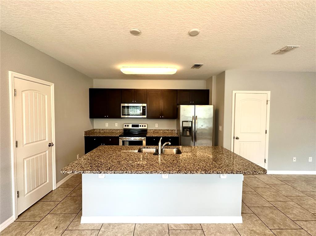 A kitchen features dark wood cabinets, granite countertops, a large island, and stainless steel appliances — 16350 TURNING TIDE WAY, WINTER GARDEN, FL