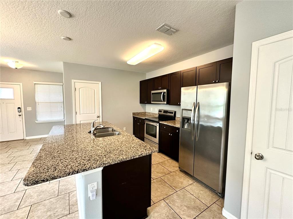 A kitchen features dark wood cabinets, granite countertops, stainless steel appliances, and a center island — 16350 TURNING TIDE WAY, WINTER GARDEN, FL