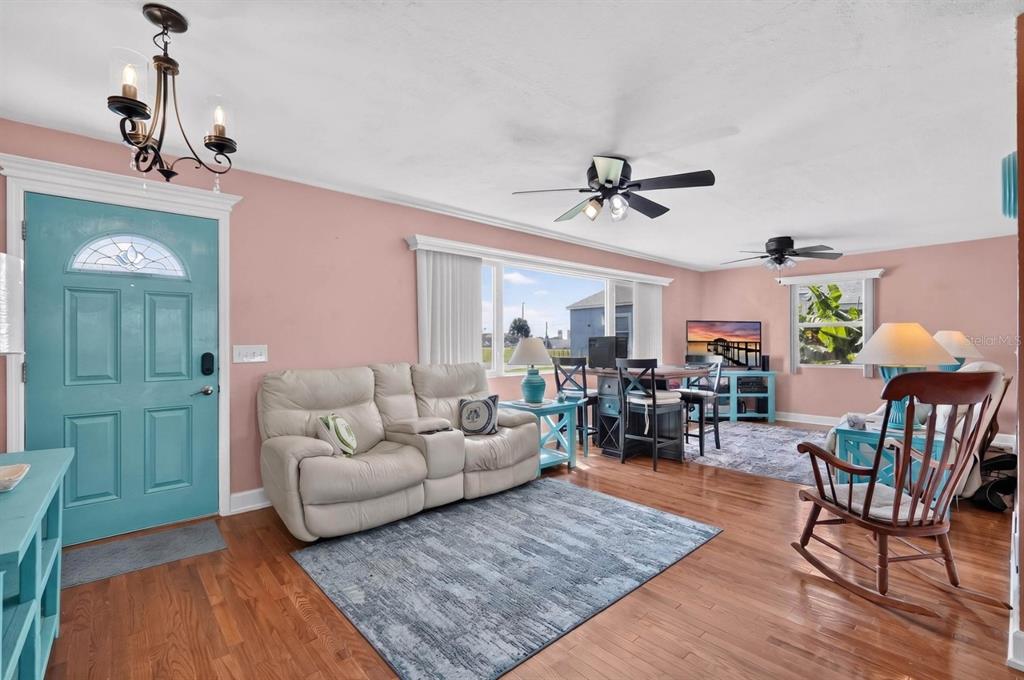 A living room features pink walls, a teal front door, hardwood floors, and a ceiling fan — 1910 MARILYN STREET, DAYTONA BEACH, FL