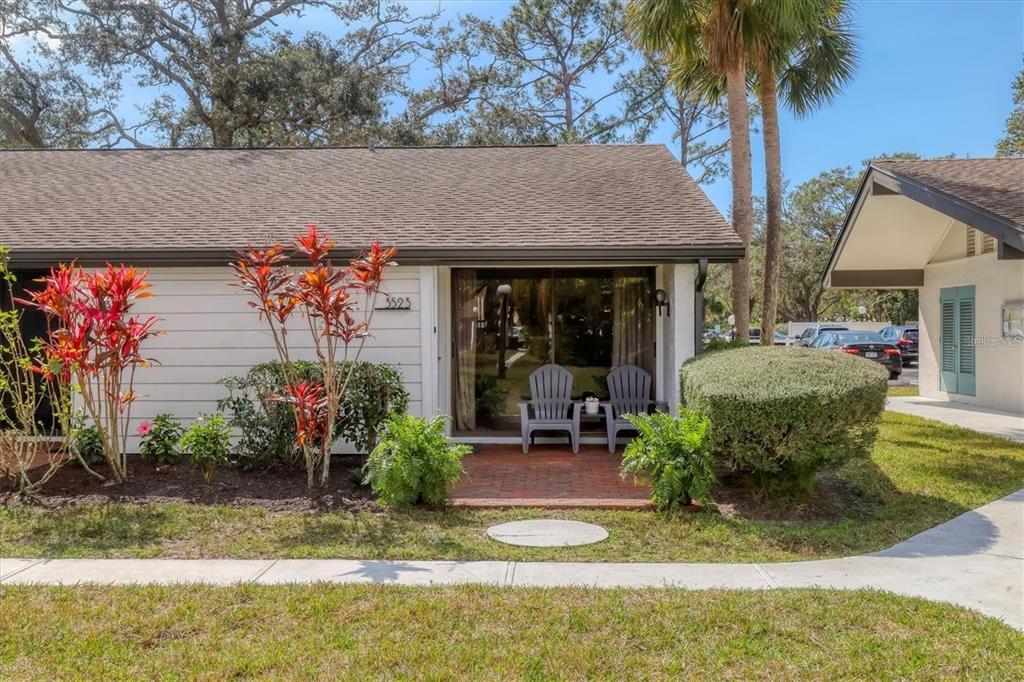A single-story residential unit features a brick patio, sliding glass doors, and tropical landscaping — 3523 LONGMEADOW UNIT 12, SARASOTA, FL