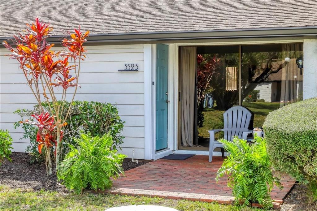 A brick patio leads to a blue front door and a sliding glass door with seating — 3523 LONGMEADOW UNIT 12, SARASOTA, FL