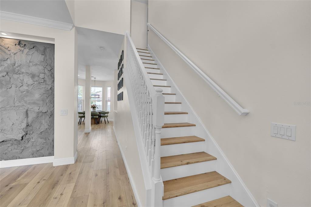 A wooden staircase with white railings leads upward next to a textured accent wall — 1250 LORETTO CIRCLE, ODESSA, FL