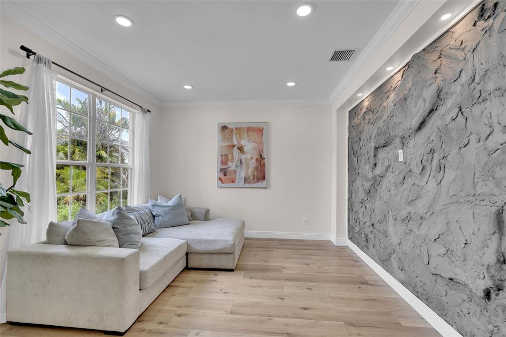 A living room features a textured gray accent wall, light wood flooring, and a sectional sofa — 1250 LORETTO CIRCLE, ODESSA, FL