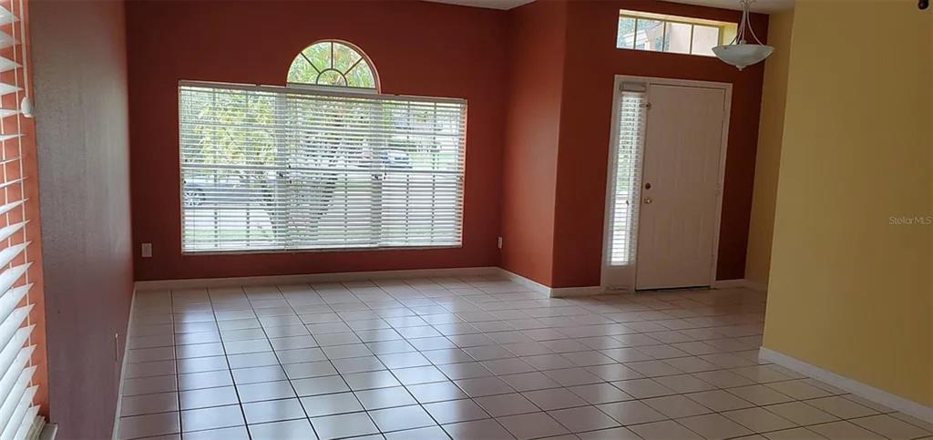 An empty room with white tiled floors, orange walls, and a large window with blinds — 4629 RIVERTON DRIVE, ORLANDO, FL