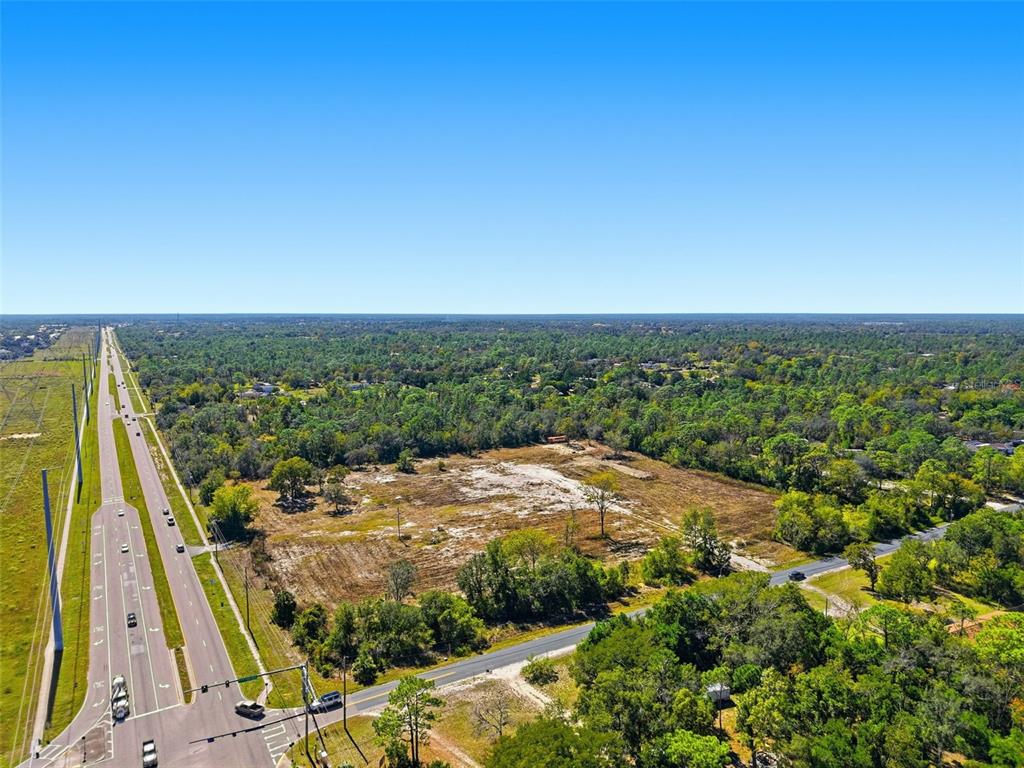 An aerial view shows a cleared, undeveloped lot bordered by a highway and wooded areas — 9247 SUNSHINE GROVE ROAD, BROOKSVILLE, FL