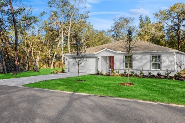 A single-story white house with a two-car garage sits on a grassy lot with trees — 11334 N FUEGO DRIVE, CITRUS SPRINGS, FL