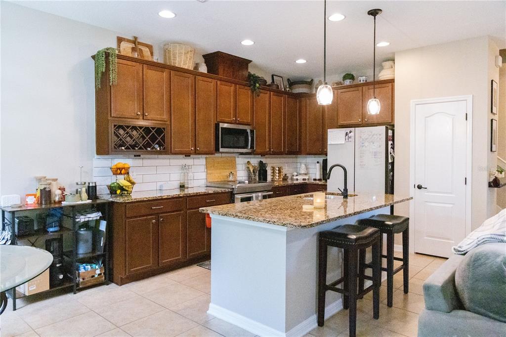 A kitchen features brown wooden cabinets, granite countertops, a central island, and stainless steel appliances — 2675 RIVER LANDING DRIVE, SANFORD, FL