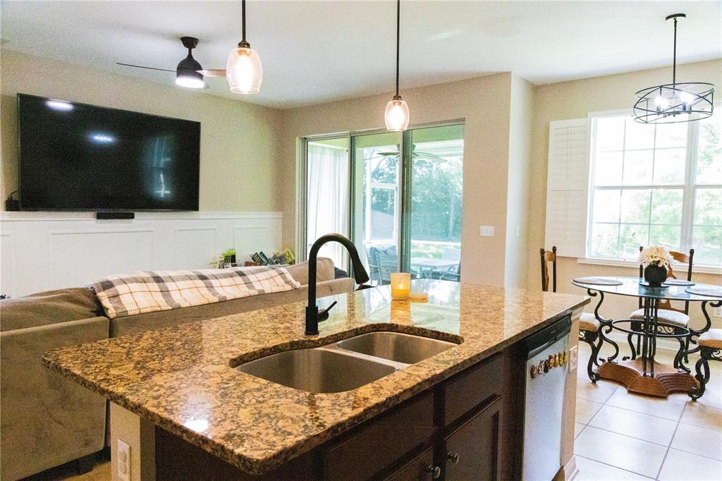 A kitchen island with a granite countertop and sink overlooks a living area and dining space — 2675 RIVER LANDING DRIVE, SANFORD, FL