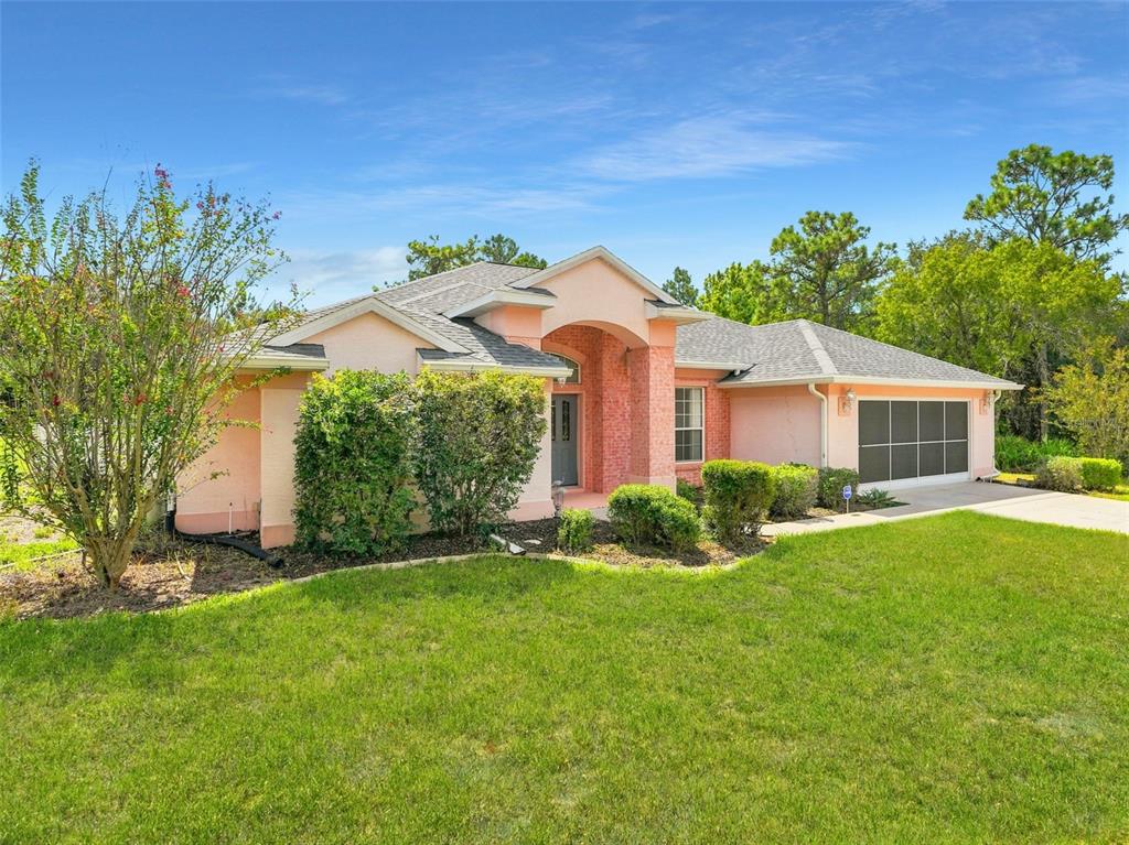A single-story peach-colored house with a brick entryway, gray roof, and a screened garage door — 56 OAK VILLAGE BOULEVARD, HOMOSASSA, FL