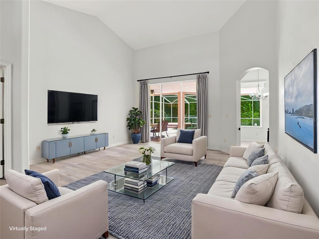 A living room with high ceilings, a television, a sofa, two armchairs, and sliding glass doors — 56 OAK VILLAGE BOULEVARD, HOMOSASSA, FL