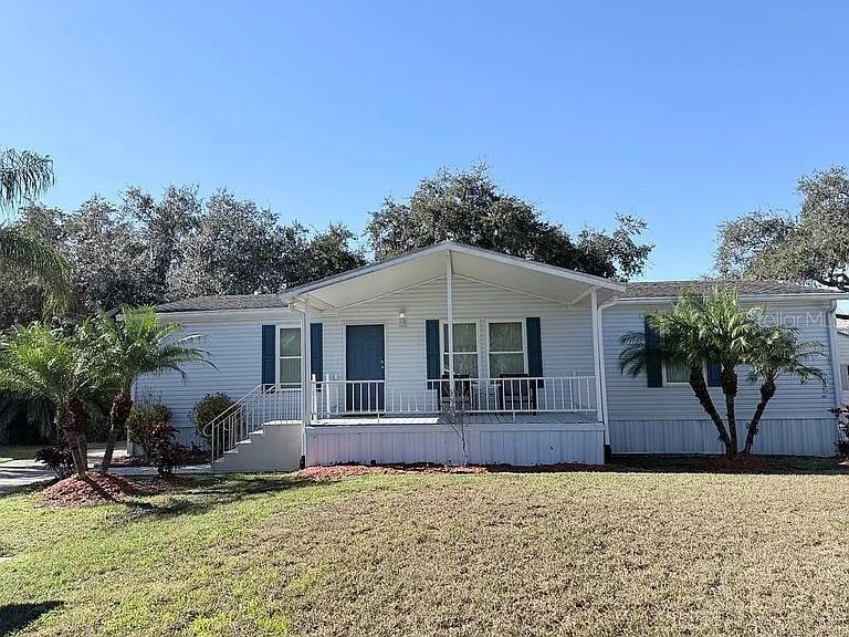 A light-colored manufactured home features a front porch, blue shutters, and two palm trees — 2086 STARBOARD DRIVE, GENEVA, FL