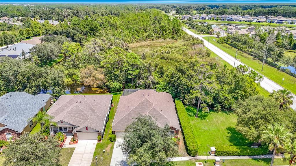 An aerial view shows two suburban houses with shingled roofs, driveways, and surrounding green landscaping — 7220 NIGHT HERON DRIVE, LAND O LAKES, FL