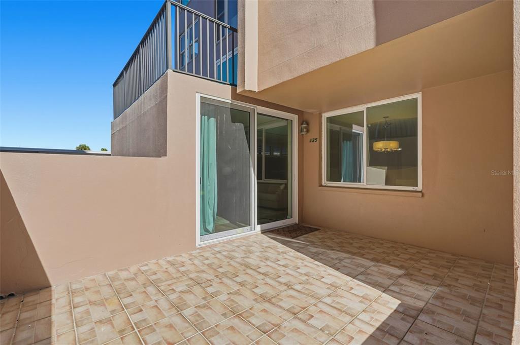 A tiled patio area features a sliding glass door and a window under an overhang — 632 EDGEWATER DRIVE UNIT 135, DUNEDIN, FL