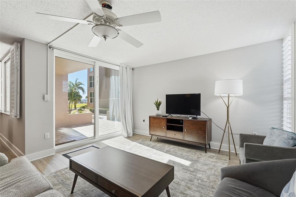 A living room features a ceiling fan, a television on a wooden console, and sliding doors — 632 EDGEWATER DRIVE UNIT 135, DUNEDIN, FL
