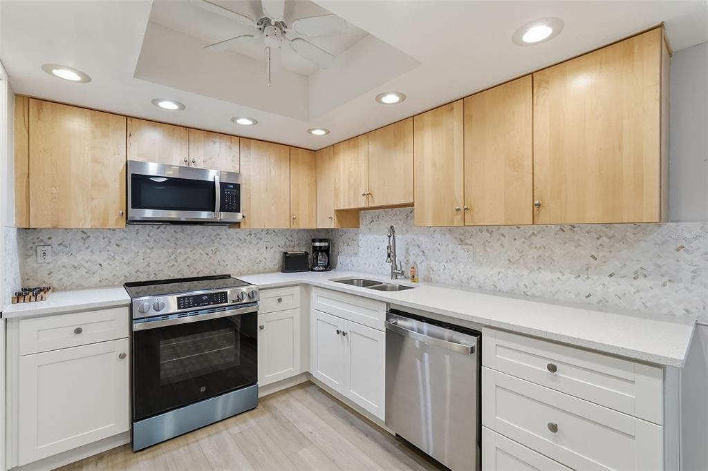 A kitchen features white lower cabinets, light wood upper cabinets, stainless steel appliances, and backsplash — 632 EDGEWATER DRIVE UNIT 135, DUNEDIN, FL