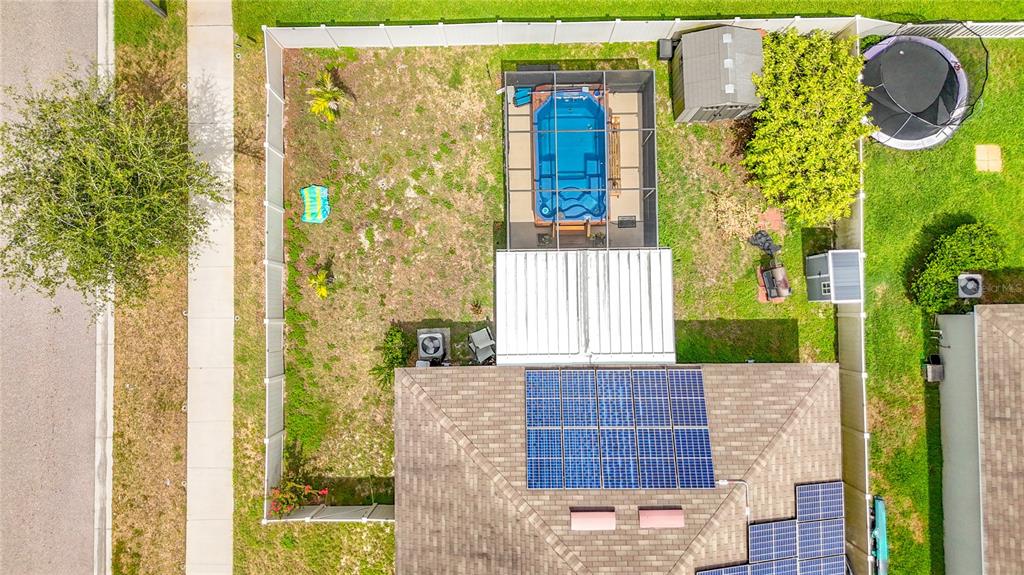 An aerial view shows a fenced backyard with a pool enclosure, solar panels, and trampoline — 102 CASCADE BEND DRIVE, RUSKIN, FL
