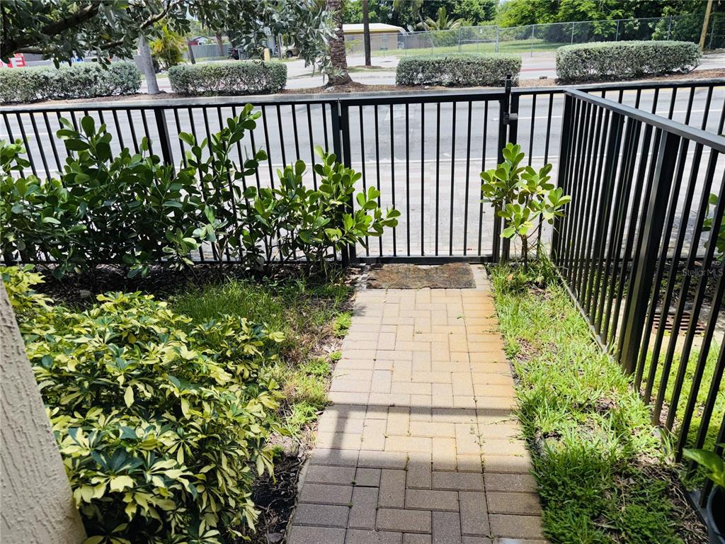 A paved walkway leads to a black metal gate surrounded by green shrubs and grass — 2132 NW 6TH STREET, FORT LAUDERDALE, FL