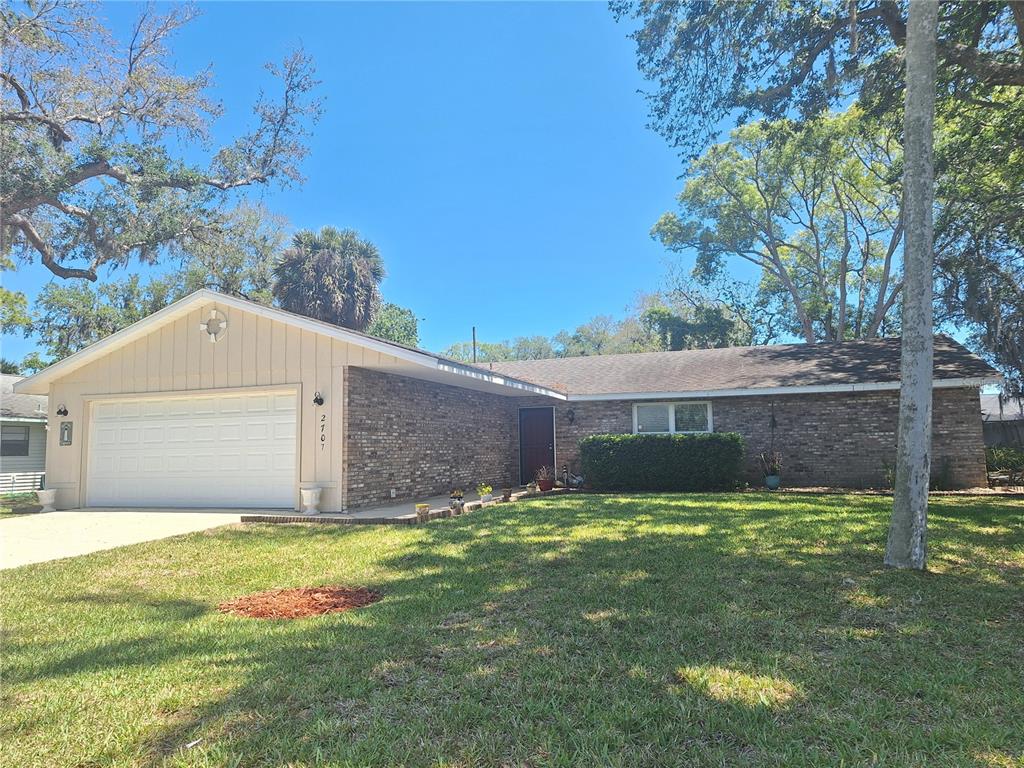 A single-story brick house with a two-car garage and a large front lawn — 2707 PINE TREE DRIVE, EDGEWATER, FL
