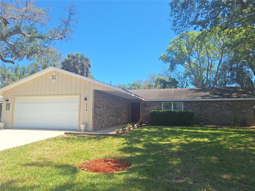 A single-story brick and siding house with a two-car garage and a front lawn — 2707 PINE TREE DRIVE, EDGEWATER, FL