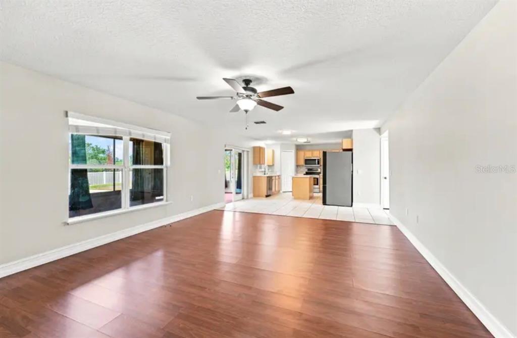 An open-concept living room with wood-look flooring leads into a kitchen with light wood cabinets — 507 GRANITE CIR, CHULUOTA, FL