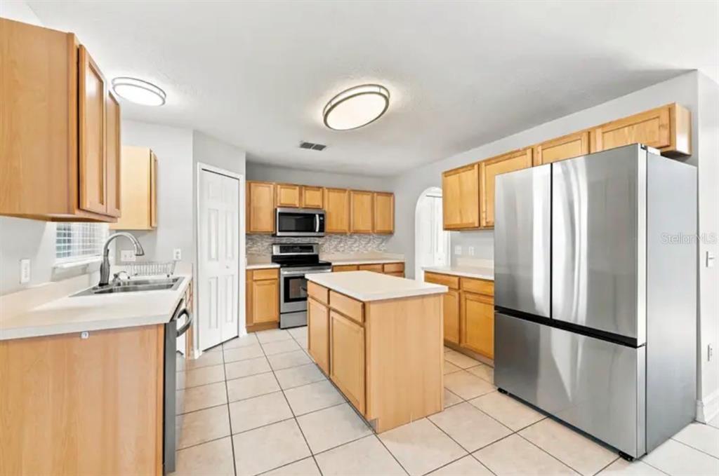 A kitchen with light wood cabinets, stainless steel appliances, a center island, and tile flooring — 507 GRANITE CIR, CHULUOTA, FL