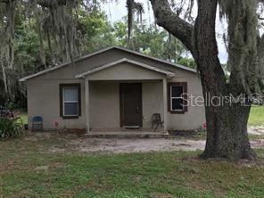 A single-story house with a covered front porch sits under a large oak tree — 1603 ROSE LANE, EUSTIS, FL