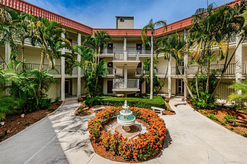 An outdoor courtyard features a central tiered fountain surrounded by orange flowers and palm trees — 2700 BAYSHORE BOULEVARD UNIT 2201, DUNEDIN, FL
