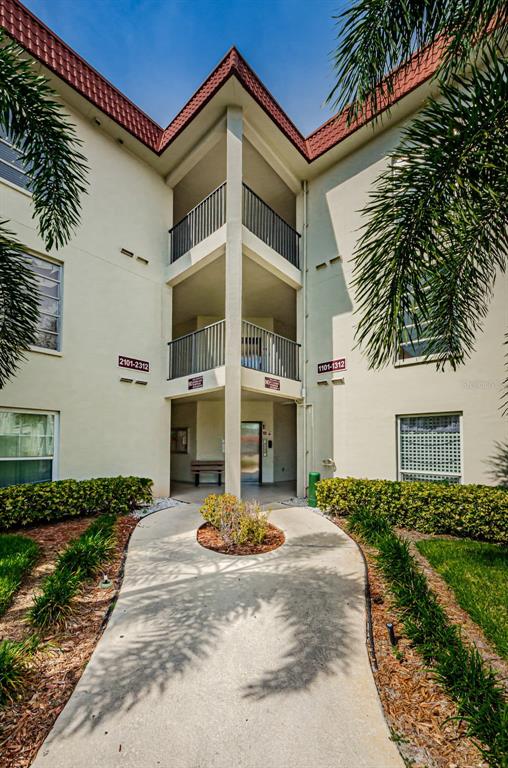 A concrete walkway leads to the entrance of a multi-story apartment building with balconies — 2700 BAYSHORE BOULEVARD UNIT 2201, DUNEDIN, FL