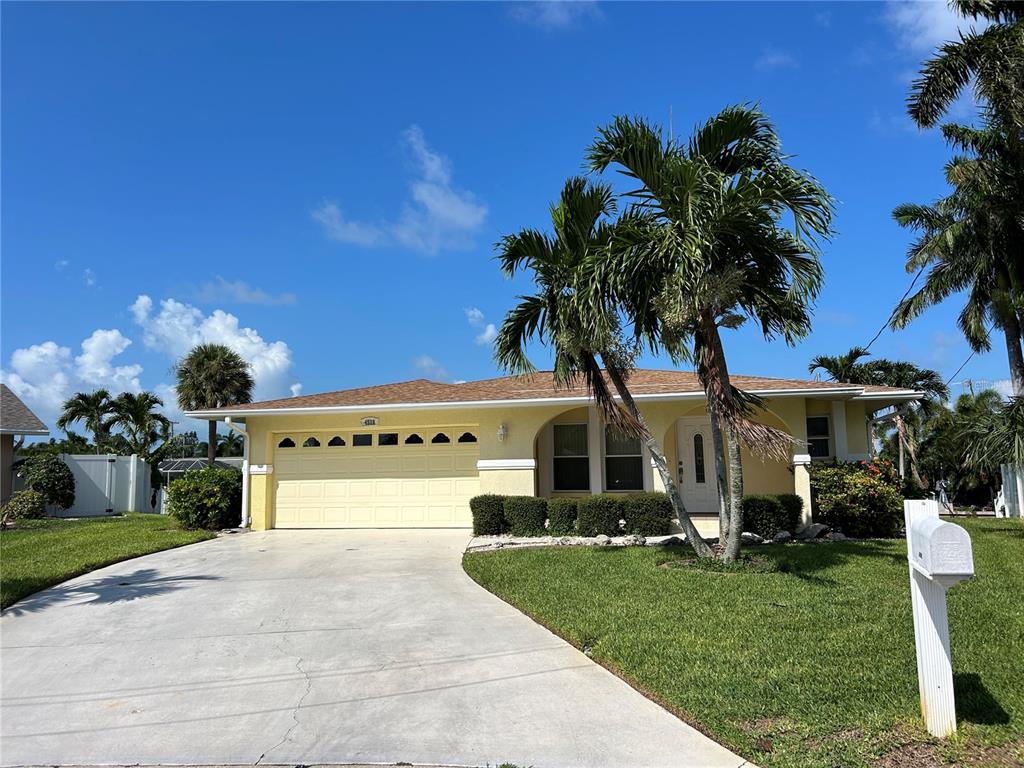 A yellow single-story house with a two-car garage, palm trees, and a concrete driveway — 4528 NASSAU ROAD, BRADENTON, FL