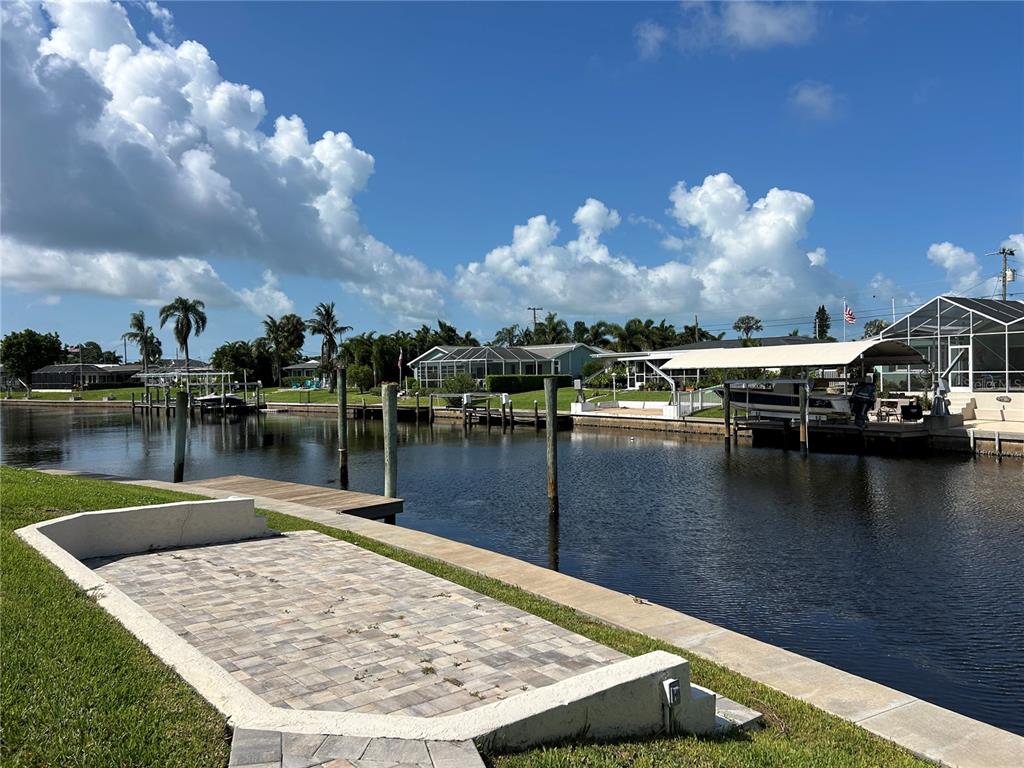 A paved patio overlooks a canal with boat docks and houses under a cloudy sky — 4528 NASSAU ROAD, BRADENTON, FL