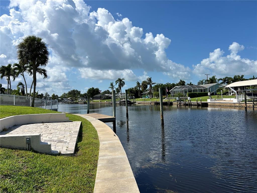 A concrete seawall borders a canal with a small wooden dock and residential homes nearby — 4528 NASSAU ROAD, BRADENTON, FL
