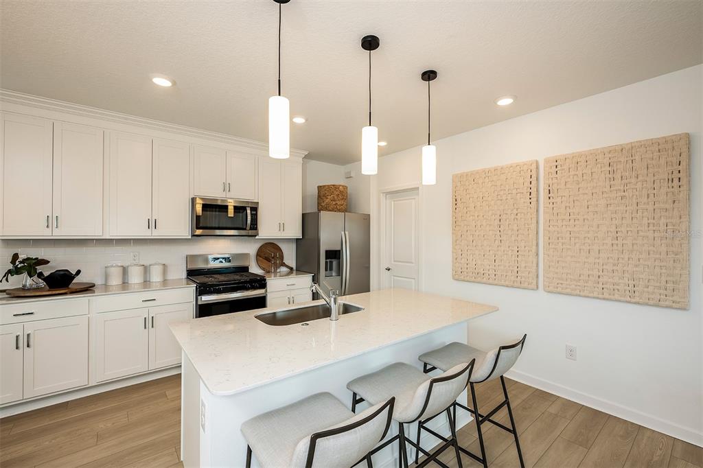 A modern kitchen features white cabinetry, a quartz island with bar seating, and pendant lighting — 5330 SPRING MAIDEN CIRCLE, APOLLO BEACH, FL
