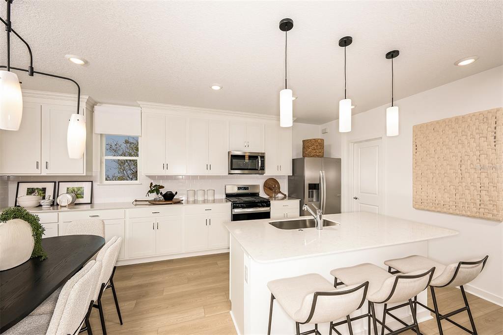 A bright kitchen features white cabinetry, a central island with bar seating, and pendant lighting — 5330 SPRING MAIDEN CIRCLE, APOLLO BEACH, FL