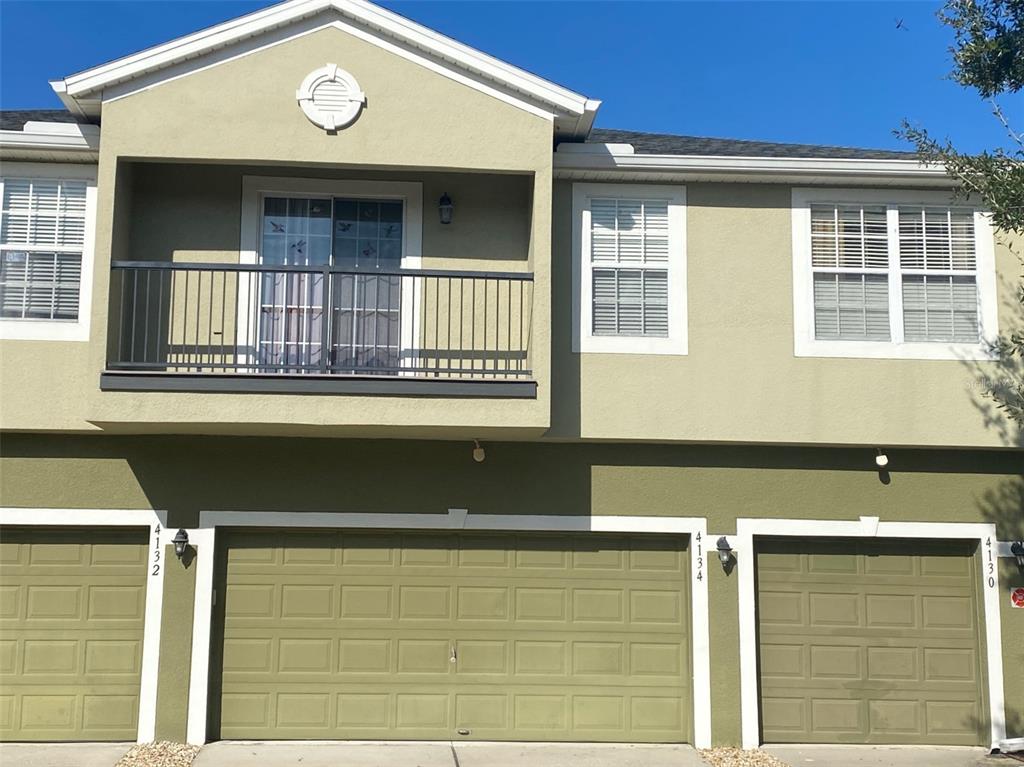 A two-story townhouse exterior features a balcony, three garage doors, and light green siding — 4130 ORANGE TREE COURT, ST CLOUD, FL