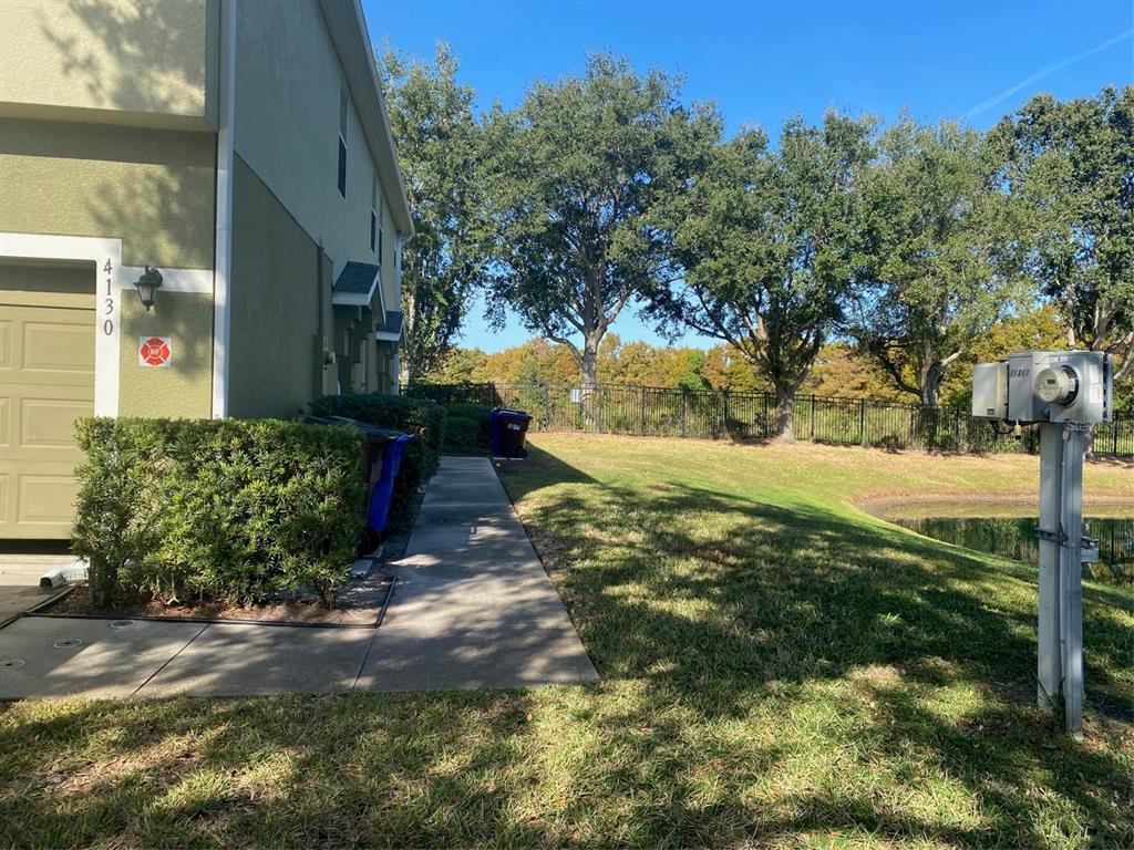 A side view of a house exterior with a sidewalk, landscaping, and a small pond — 4130 ORANGE TREE COURT, ST CLOUD, FL