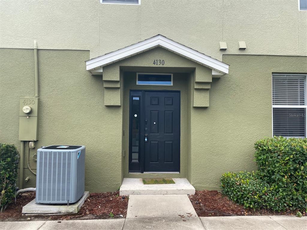 The exterior of a green townhouse features a black front door and an air conditioning unit — 4130 ORANGE TREE COURT, ST CLOUD, FL
