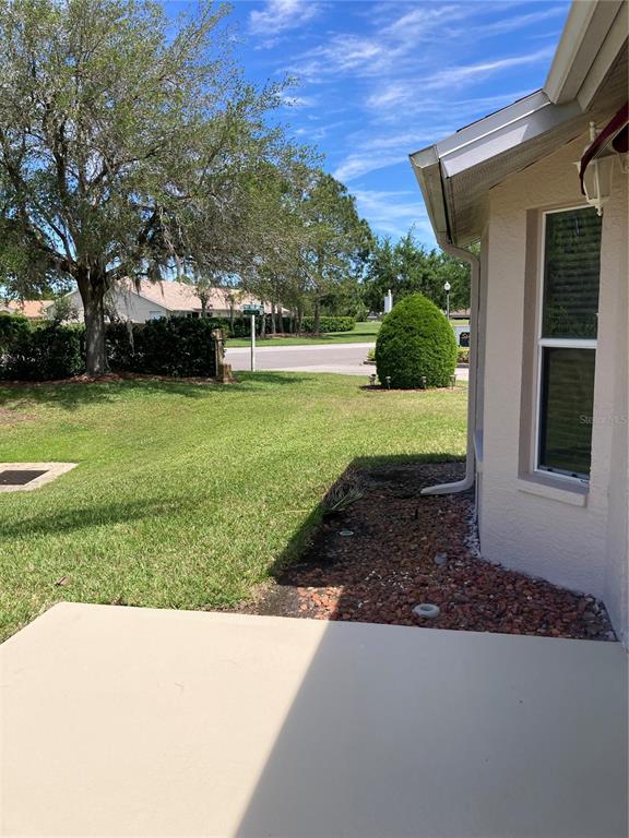 A concrete patio overlooks a grassy yard with a tree, shrubs, and a nearby street — 1327 TOLLBRIDGE COURT, TRINITY, FL