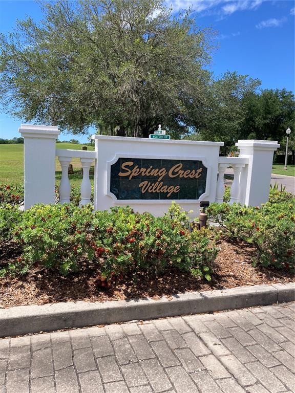A white monument sign for Spring Crest Village stands behind a landscaped garden bed — 1327 TOLLBRIDGE COURT, TRINITY, FL