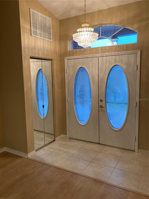 An entryway features a crystal chandelier, double front doors with oval glass, and mirrored closet doors — 1327 TOLLBRIDGE COURT, TRINITY, FL