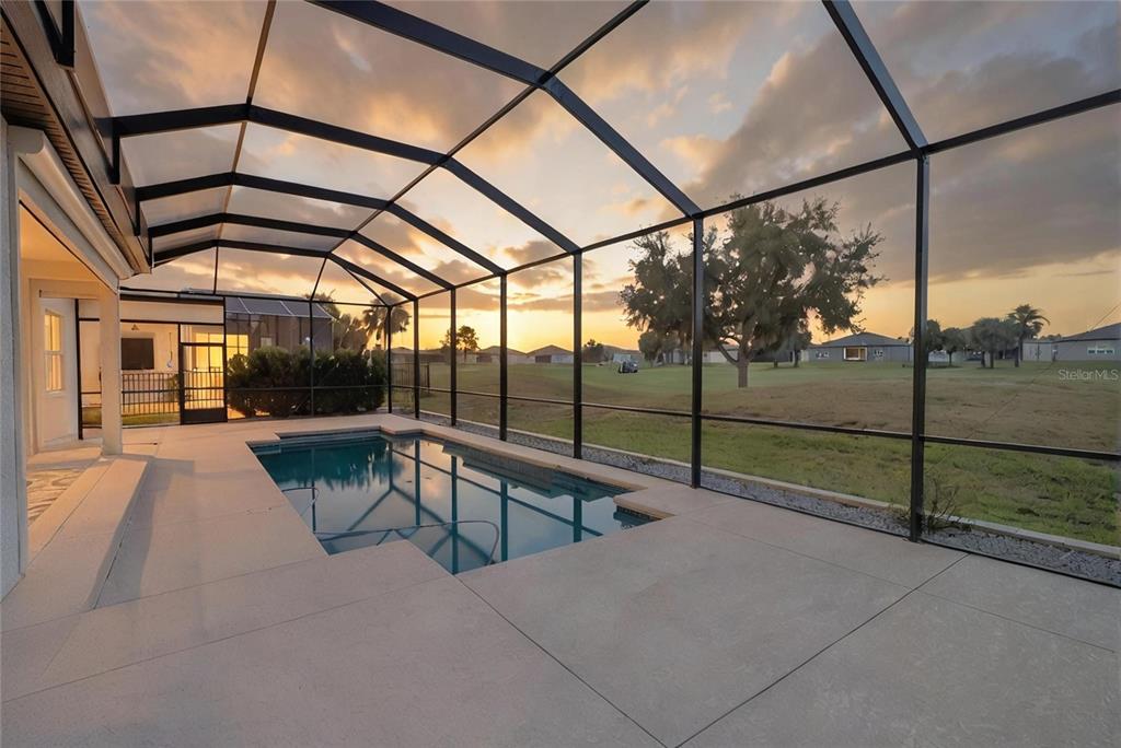 A screened-in patio features a rectangular swimming pool overlooking a grassy golf course at sunset — 6107 SW 86TH CIRCLE, OCALA, FL