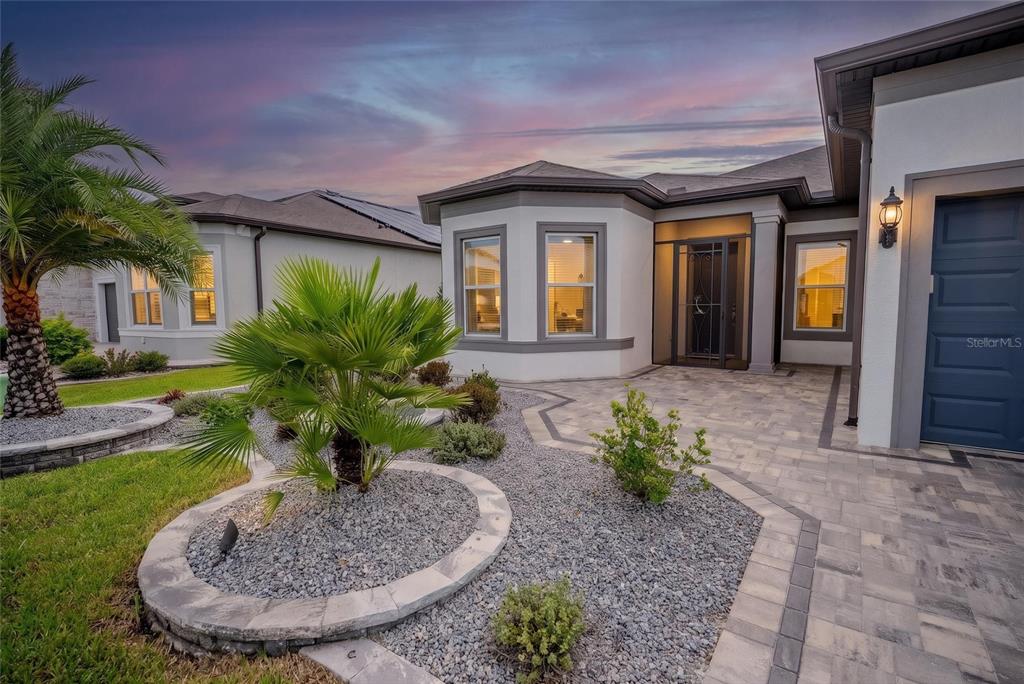 A modern house exterior features a paver walkway, gray gravel landscaping, and a blue door — 6107 SW 86TH CIRCLE, OCALA, FL
