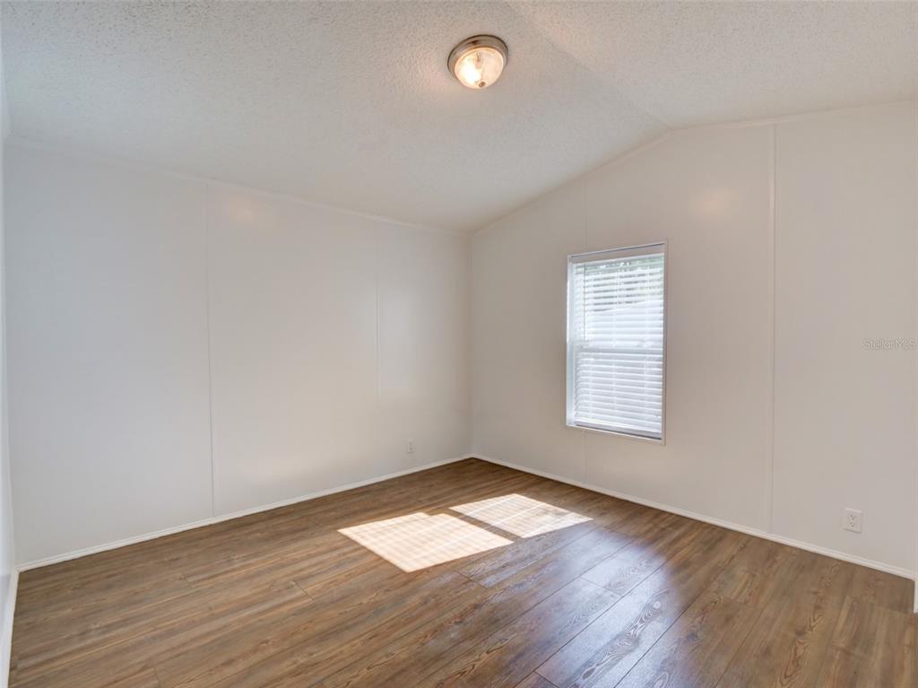An empty bedroom features white walls, wood-look flooring, a single window, and a ceiling light — 26007 HECKMAN DRIVE, BROOKSVILLE, FL