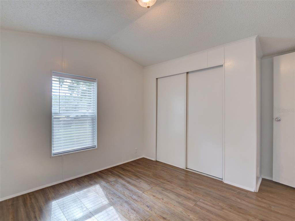 A bedroom with white walls, wood-look flooring, a window with blinds, and a sliding closet — 26007 HECKMAN DRIVE, BROOKSVILLE, FL