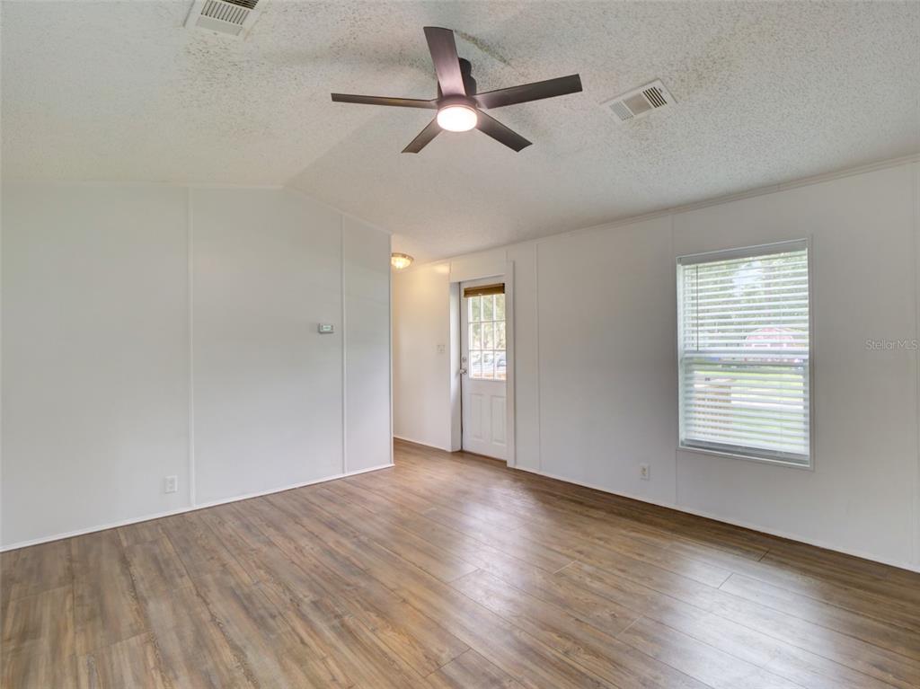 An empty room with wood-look flooring, white walls, a ceiling fan, and a glass-paneled door — 26007 HECKMAN DRIVE, BROOKSVILLE, FL